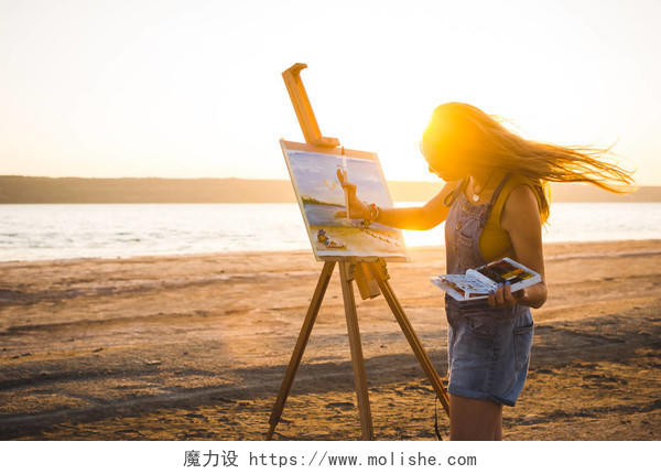 年轻女子艺术家在露天沙滩上画风景画